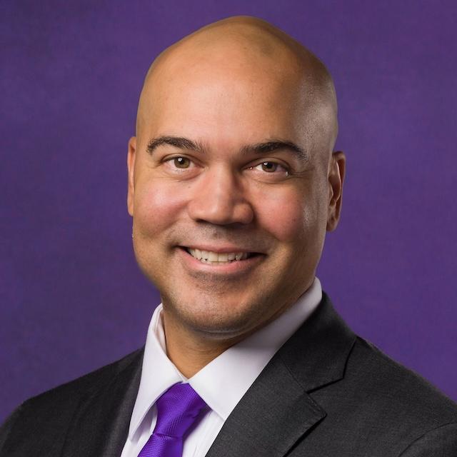 Photo of Dr. Bernard Rousseau, dean of Harris College announced in 2026. He is wearing a white button-down collared shirt with a purple tie and black jacket, with a purple background