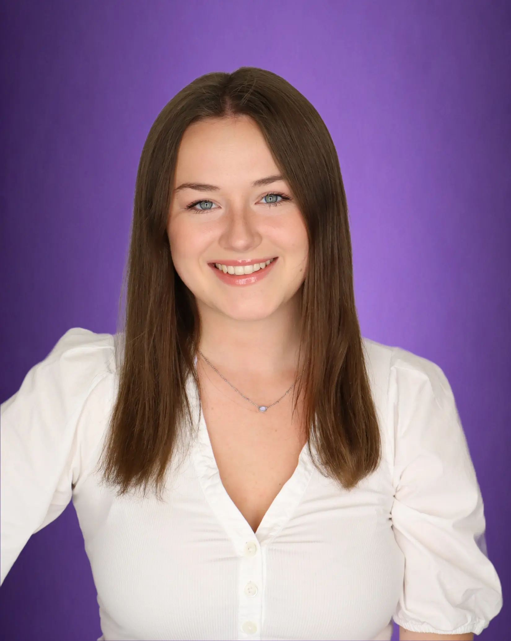 A woman, smiling, wearing a white blouse with a purple background
