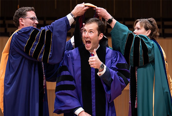 Student at hooding ceremony with faculty members.